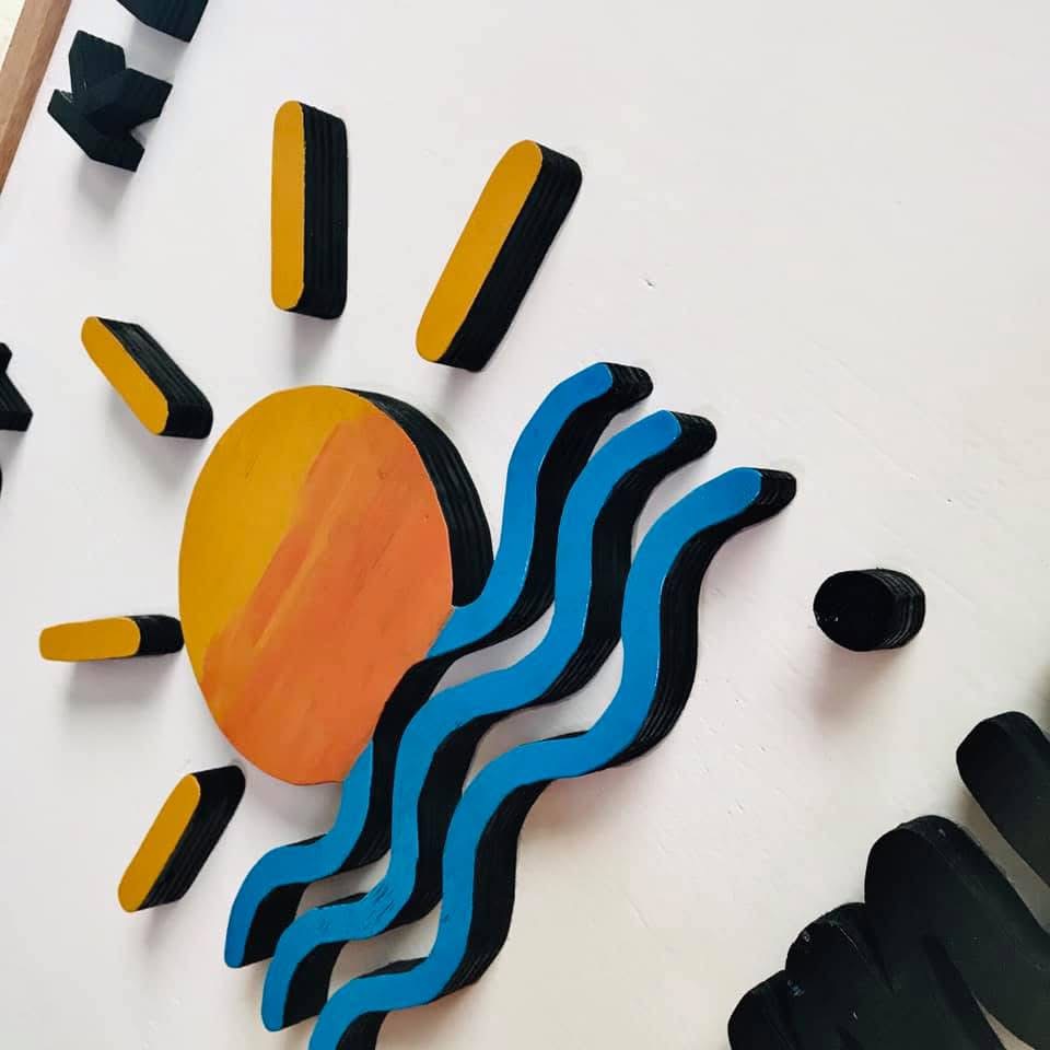 Hand-painted wooden sun and blue wave cut-outs mounted on a white board