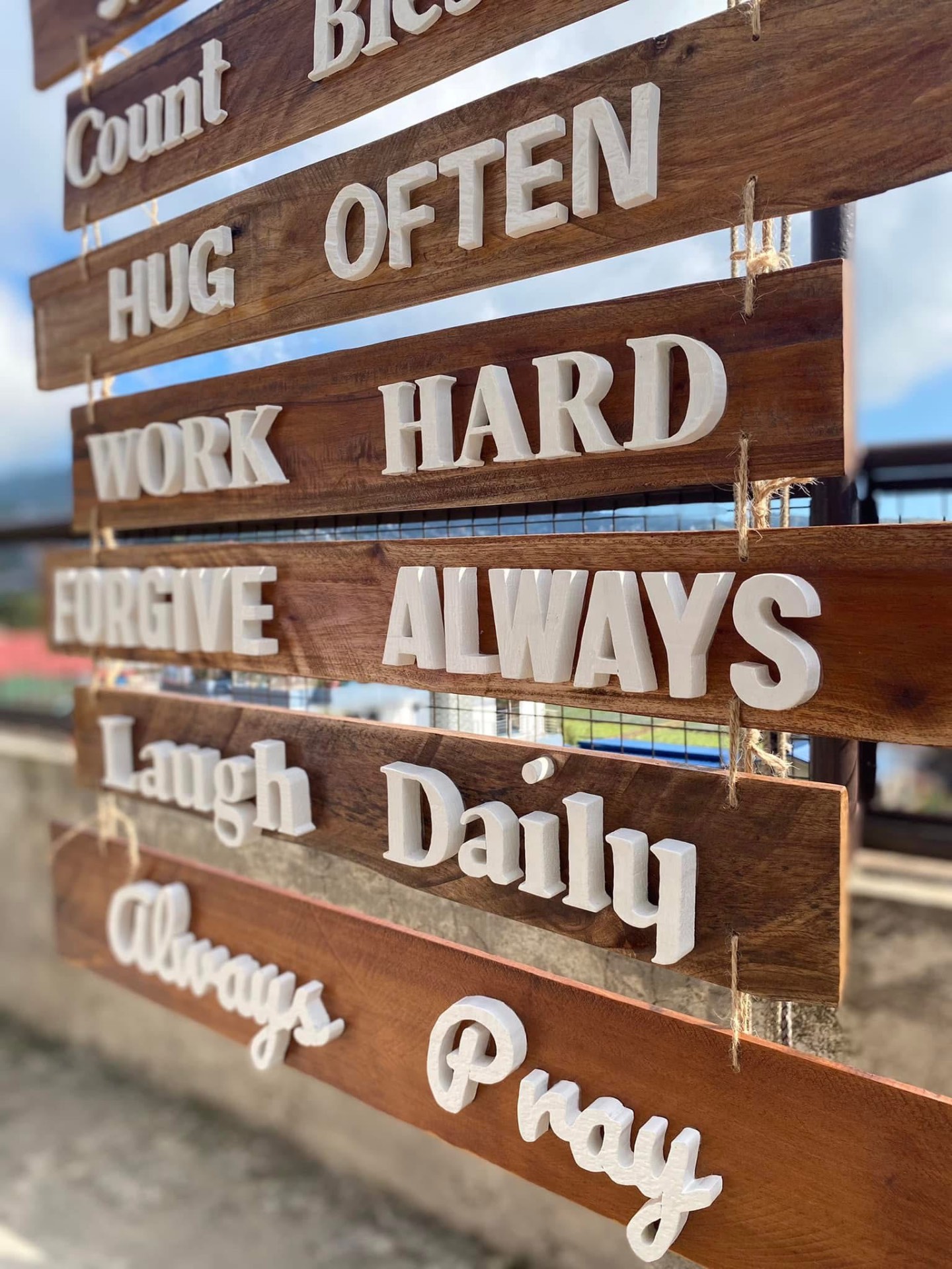Stacked hanging wooden slats with white letters reading count blessings, hug often, work hard, forgive always, laugh daily, always pray