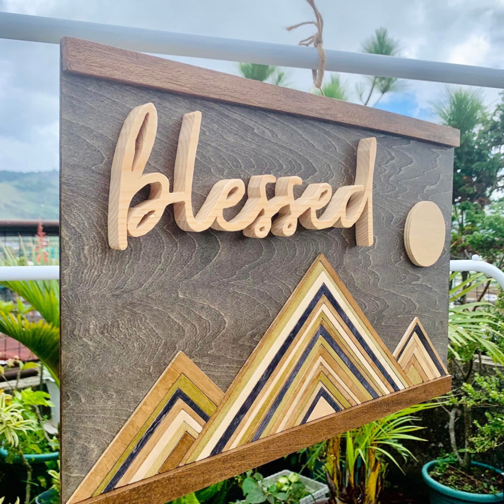 Grey stained wood board with raised 'blessed' script above layered chevron mountains and a wooden moon