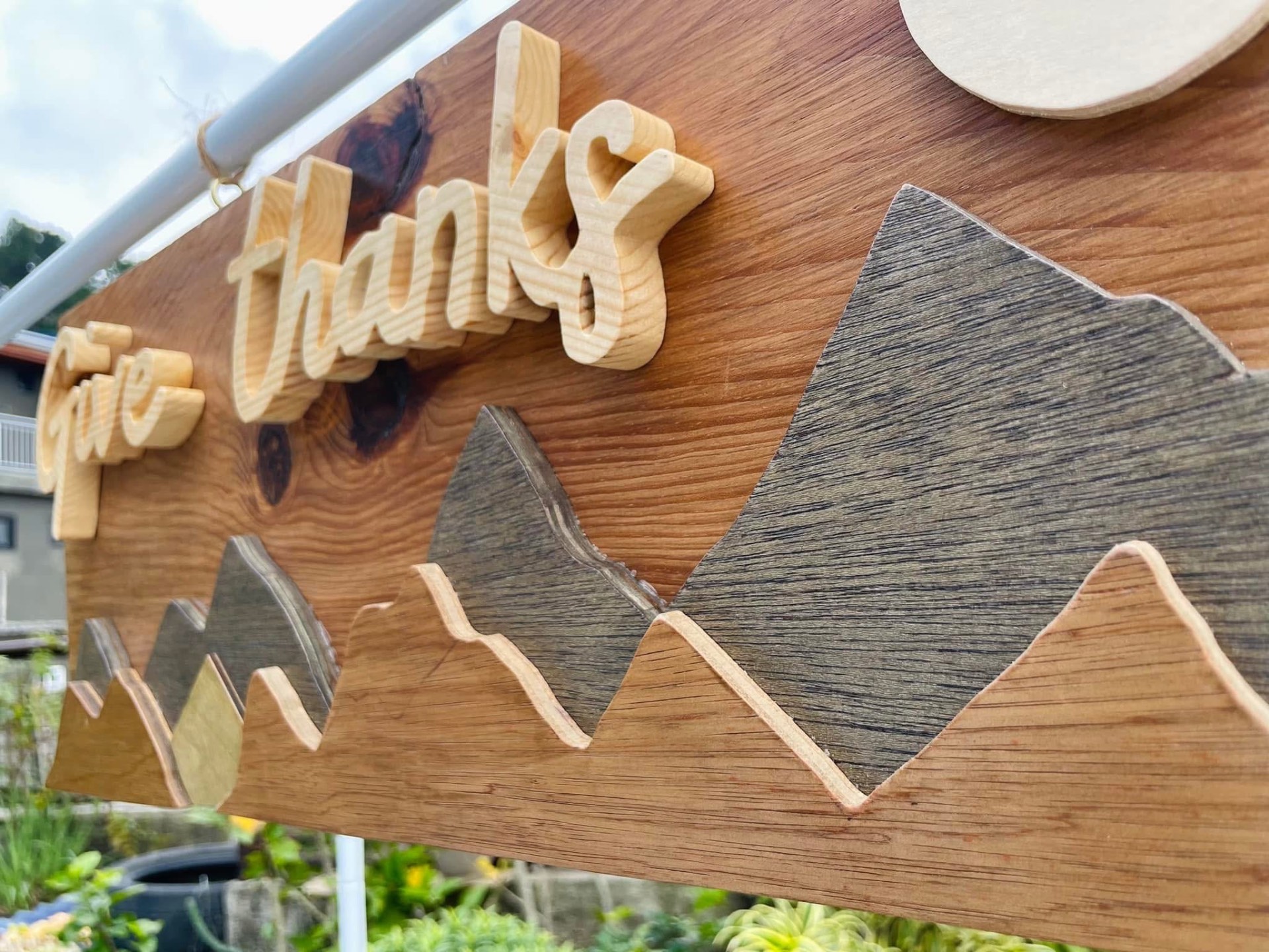 Long wooden panel with raised script 'give thanks' above layered wooden mountain ridges